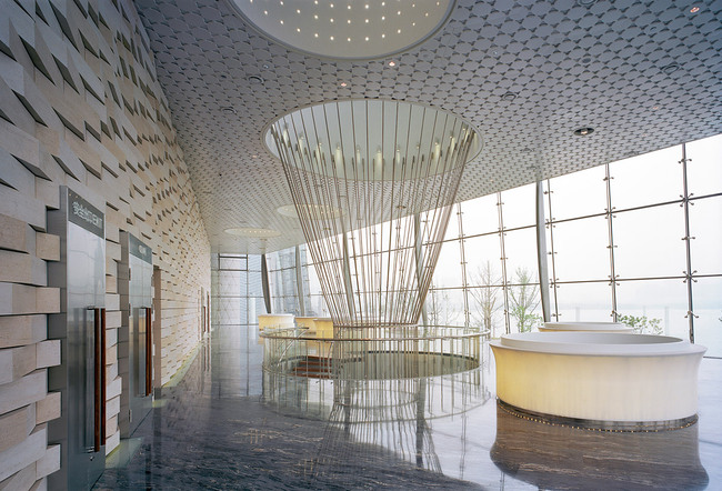 The lake side lobby of the small auditorium. This elevated space is providing great views over the Wuli Lake. The auditorium is accessed via two levels which are connected by a suspended spiral staircase. The entrance wall to the auditorium is covered with special designed CNC cut stone blocks relating to the angulated black brick wall inside the auditorium. (Photo: Jussi Tiainen)